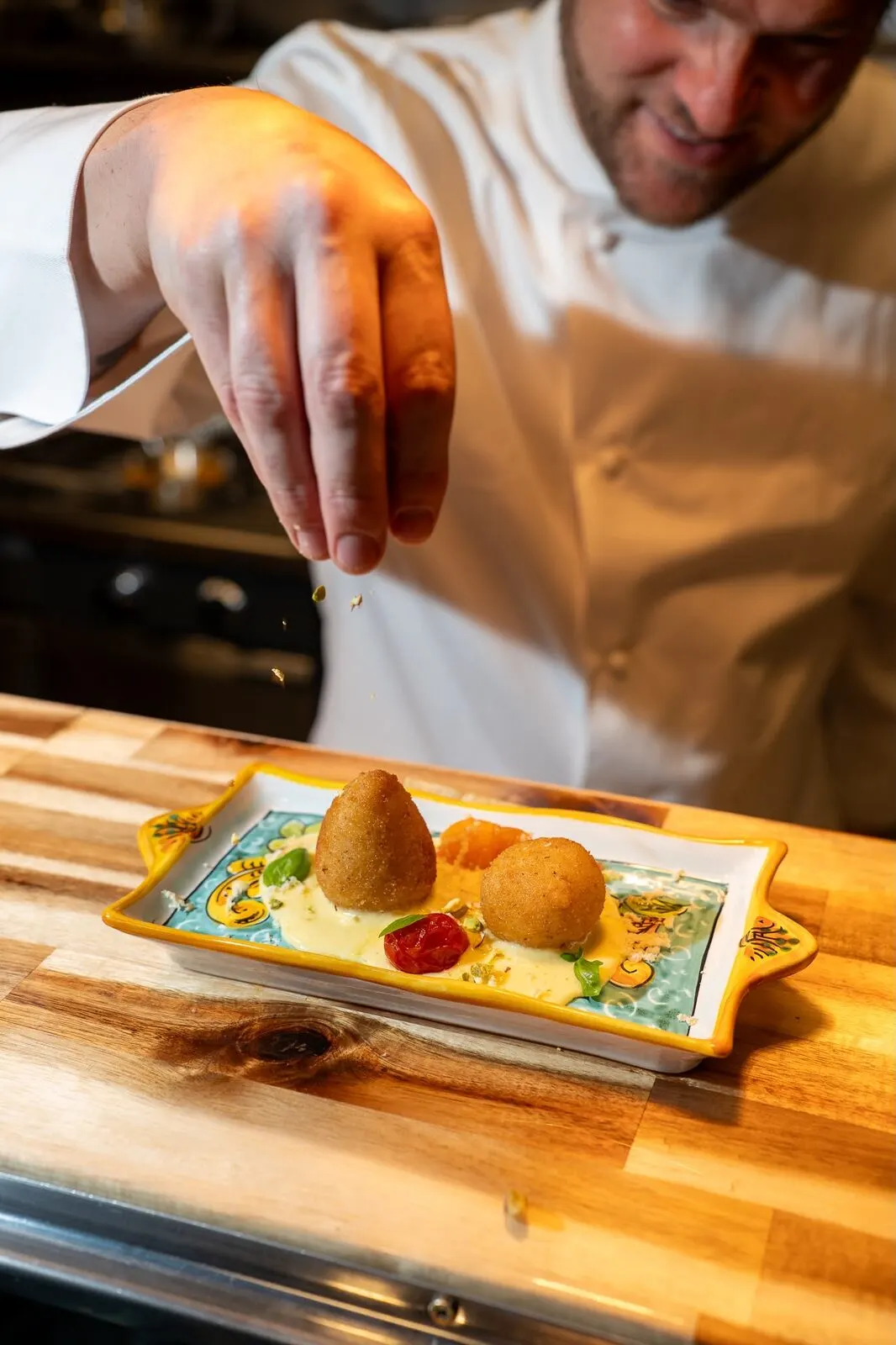 Arancini being plated onto a painted ceramic tray