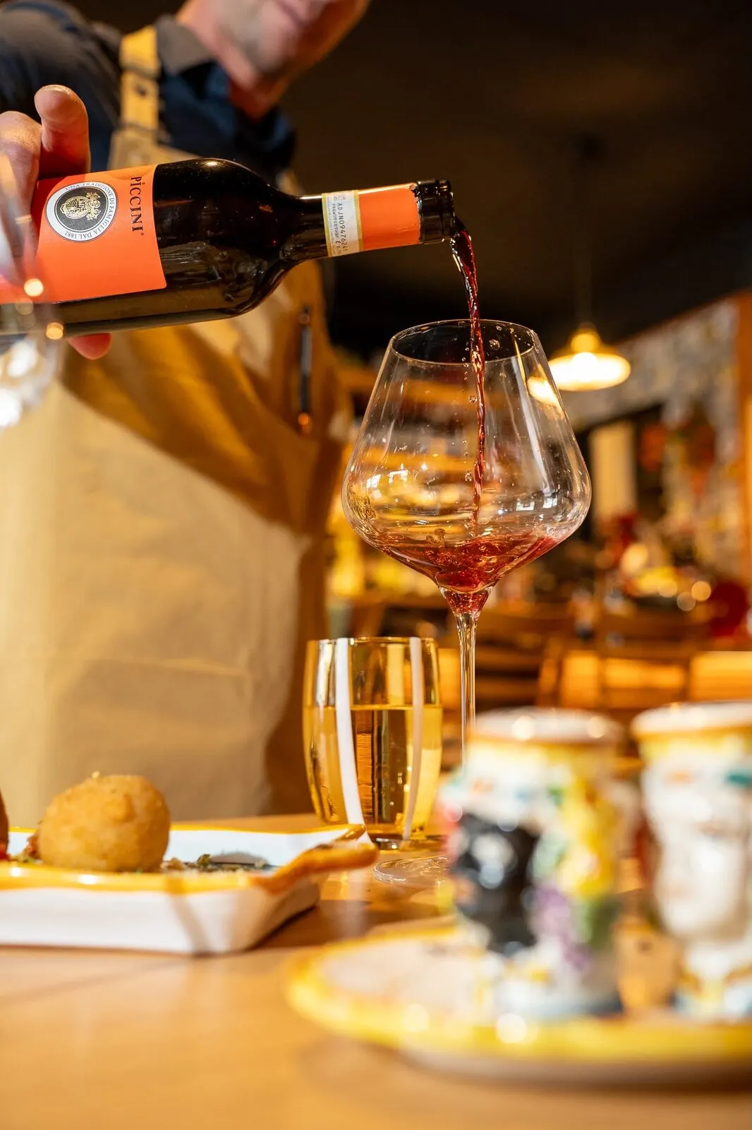 A bottle of red being poured into a glass at the table